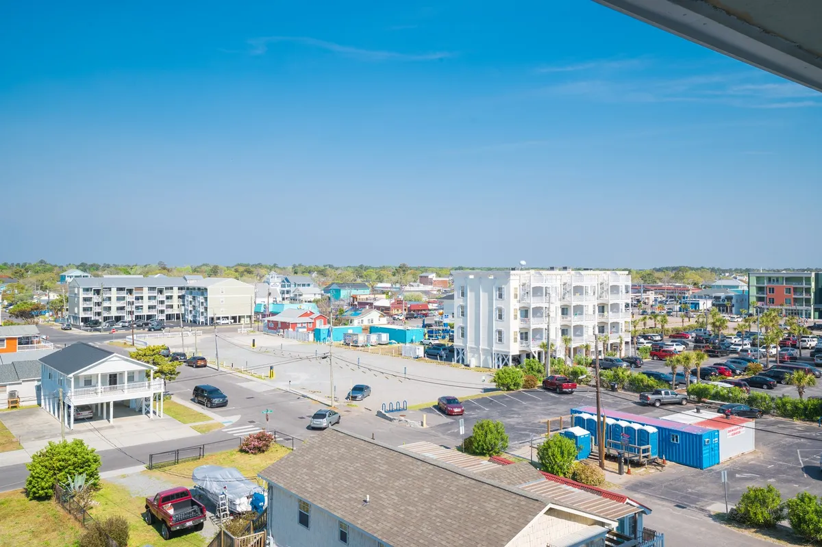 A vibrant streetscape with colorful buildings, bustling parking areas, and nearby green spaces, hinting at the lively attractions around the Carolina Beach Boardwalk. The scene suggests easy access to local shops, eateries, and entertainment just a short walk away.