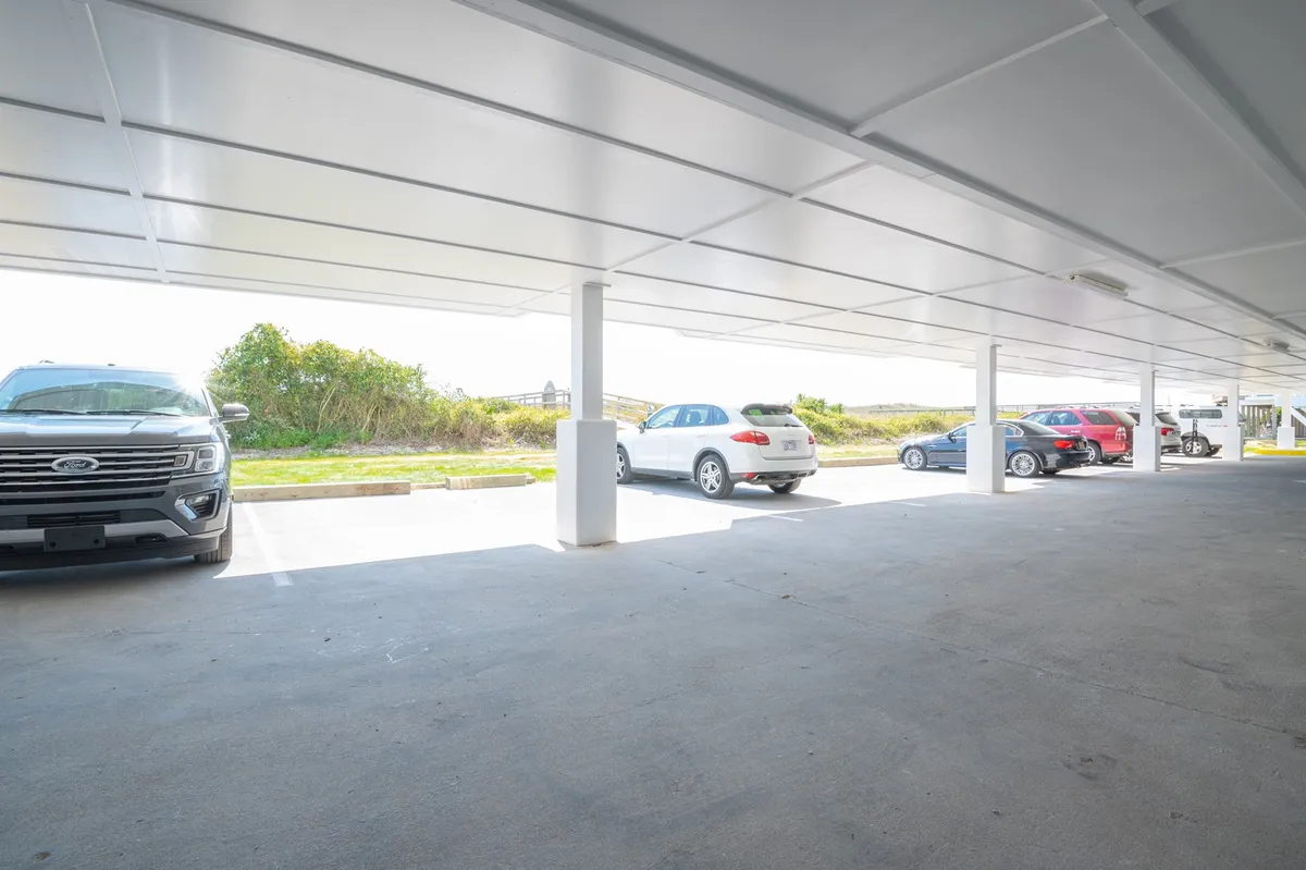 A covered parking structure with vehicles parked inside and a landscape visible in the background. The image conveys convenient access to the building, suggesting an easy transition from outdoor adventures back to the comfort of the condo.