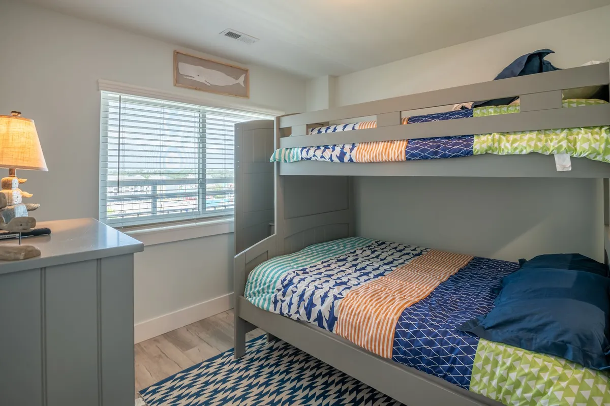 A playful and cozy guest bedroom featuring a twin-over-full bunk bed with colorful bedding. A lamp, soft rug, and inviting decor create a welcoming atmosphere for children or families. The arrangement supports both sleep and play, with a focus on comfort and fun.