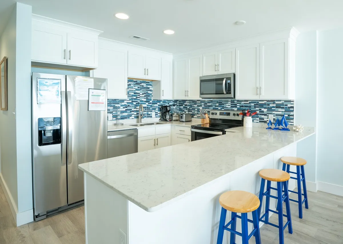 A modern kitchen featuring striking blue backsplash tiles, marble countertops, stainless steel appliances, and breakfast bar seating. The open design invites conversation and culinary creations.