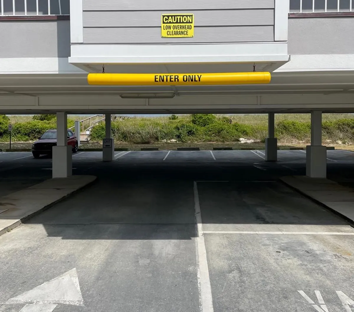 This image features an entryway marked with 'enter only' and 'low overhead clearance' signs, with several empty parking spots in view. The scene is functional and practical, emphasizing convenience and a sense of safety for arriving guests.