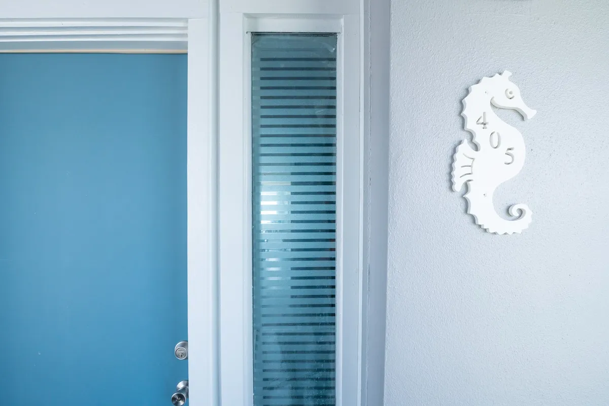 A cheerful entryway featuring a blue door with a seahorse motif and glass panel, providing a welcoming introduction to the building’s coastal ambiance.