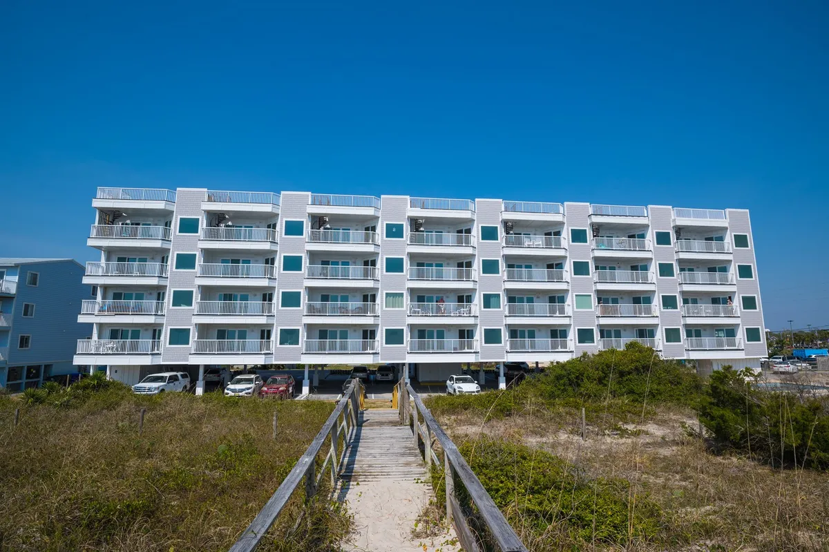 This exterior shot displays a multi-story building framed by lush vegetation, with visible walkways leading toward the beach. Balconies on multiple levels hint at the distinctive multi-level layout mentioned in the section, and the setting suggests a welcoming, social environment just steps from the sand.